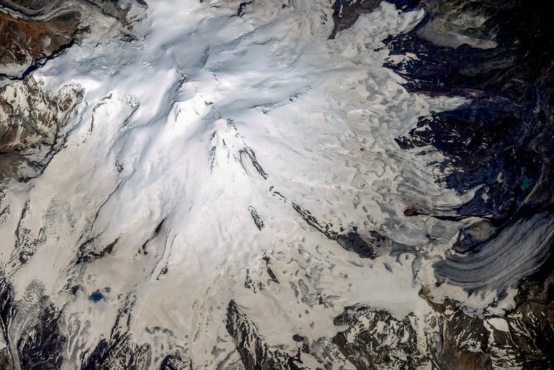 Рис. 13. На аэрофотоснимке Эльбруса хорошо видно наличие вулканических кратеров на двух вершинах (западный&nbsp;– крупнее, восточный&nbsp;– меньше). Черная нисходящая полоса справа по направлению &#171;на 4 часа&#187; - проступивший сквозь снег застывший лавовый поток&nbsp;[16]